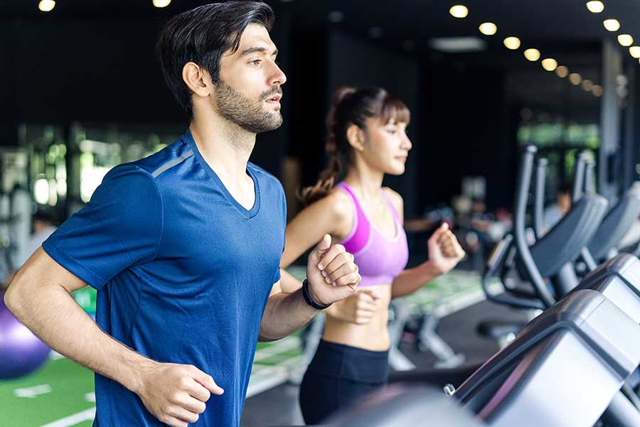 Caucasian man and beautiful Asian woman running on treadmill or running machine in fitness gym.