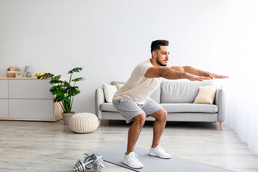 Handsome young Arab man doing squats, working out at home, full length