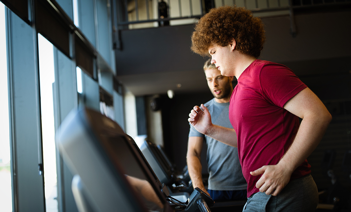 Overweight young man working out with a personal trainer at Gold's Gym.