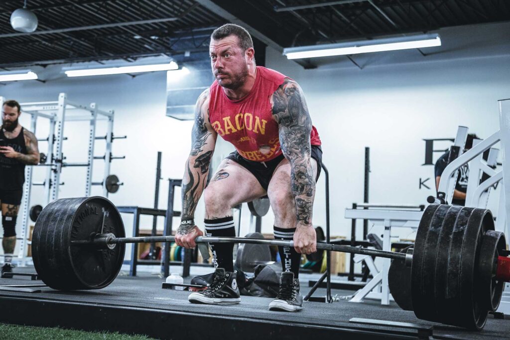 A muscled man with tattoos performs a deadlift at the gym.