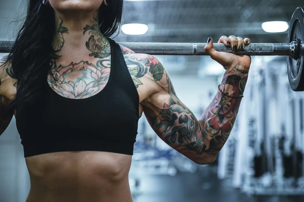 Tattooed woman carrying barbell in Coquitlam’s top powerlifting gym: Gold’s gym.