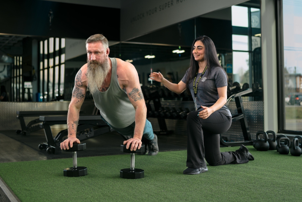 a gym member does dumbell pushups with a personal trainer at golds gym near me