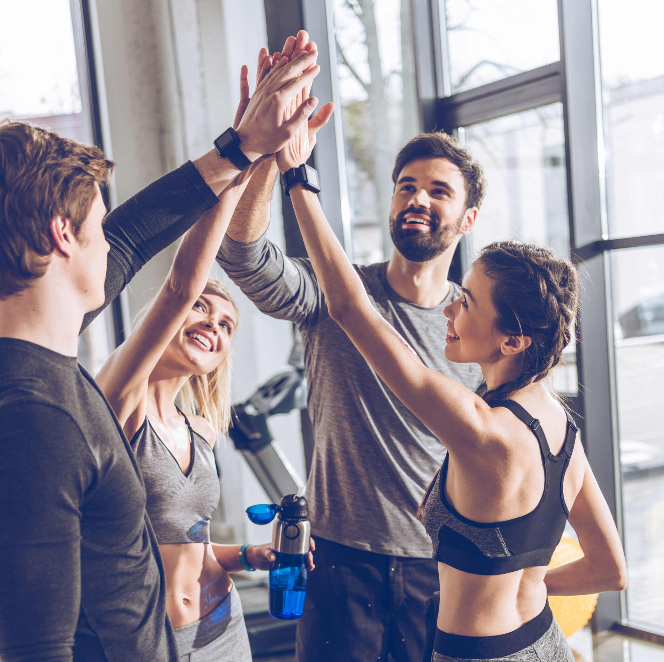 Happy young athletic people in sportswear giving high five in gym